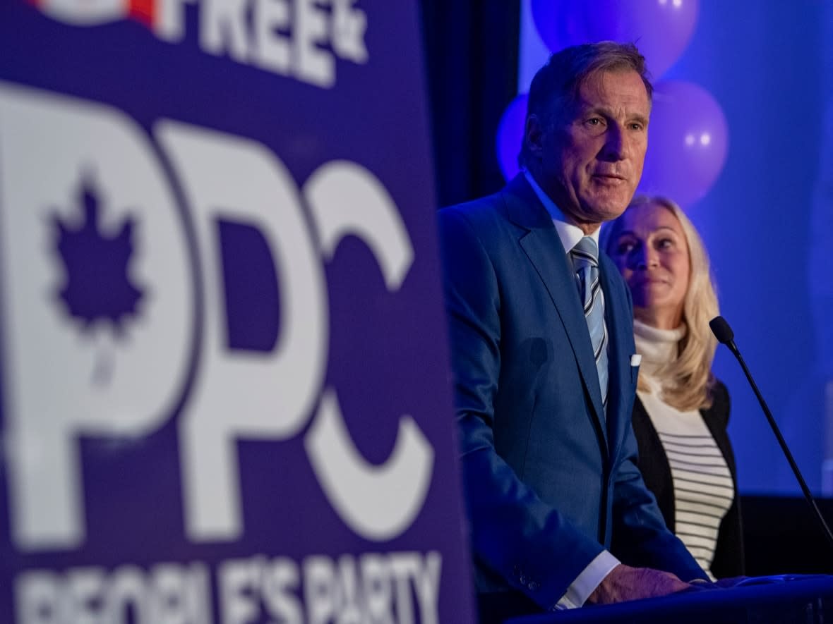 People's Party of Canada Leader Maxime Bernier, with his wife, Catherine Letarte, speaks from a podium to supporters during the PPC headquarters in Saskatoon on Sept. 20. Bernier's photo was not among the 15 maskless people at the event on election night that police posted on their website. (Liam Richards/The Canadian Press - image credit)