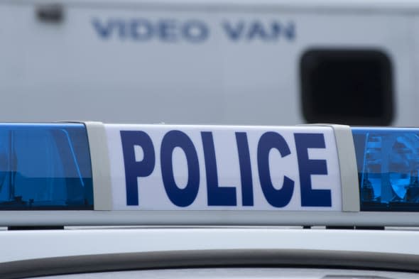 Closeup of police car sign with video unit vehicle in background.