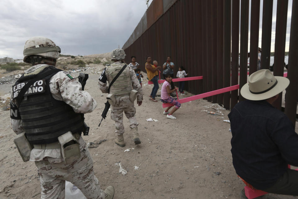 CORRECTS THE FIRST NAME OF THE PROFESSOR TO RONALD, NOT RONALDO AND THE LAST NAME OF THE PHOTOGRAPHER TO CHAVEZ, NOT TORRES - Members of the Mexican military police wearing the insignia of the new National Guard check children and people as they play seesaw installed between the border fence that divides Mexico from the United States in Ciudad de Juarez, Mexico, Sunday, July 28, 2019. The seesaw was designed by Ronald Rael, a professor of architecture in California. (AP Photo/Christian Chavez)