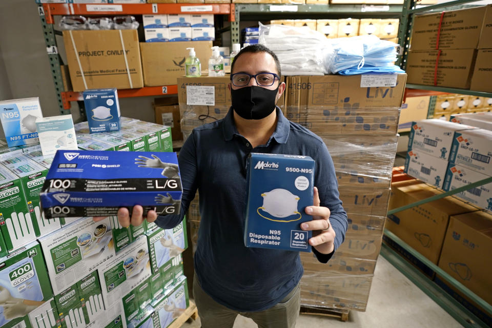 Ray Bellia holds up personal protective masks and gloves, used by medical and law enforcement professionals, in the warehouse of his Body Armor Outlet store, Wednesday, Dec. 9, 2020, in Salem, N.H. Bellia's store rapidly evolved into one of the nation's 20 largest suppliers of personal protective equipment to states this past spring, according to a nationwide analysis of state purchasing data by The Associated Press. (AP Photo/Charles Krupa)