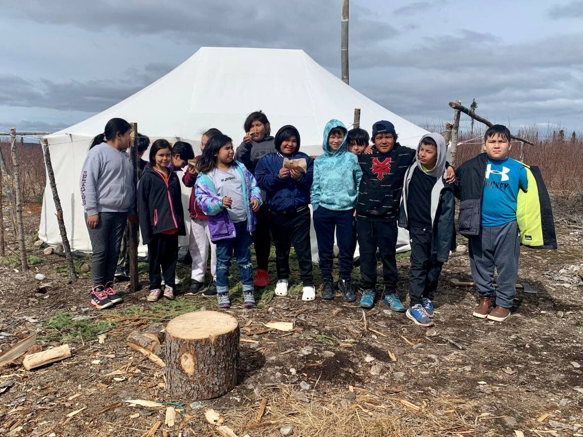 The third grade class at the Sheshatshiu Innu School in Labrador stands outside a traditional Innu tent set up behind their school on May 10. Inside, they got to watch three elders make Innu doughnuts. (Sarah Smellie/The Canadian Press - image credit)