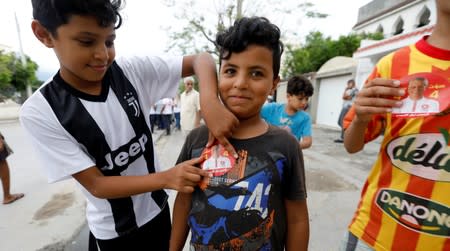 A boy puts a sticker of presidential candidate Nabil Karoui on his friend's t-shirt during a campaign in Tunis