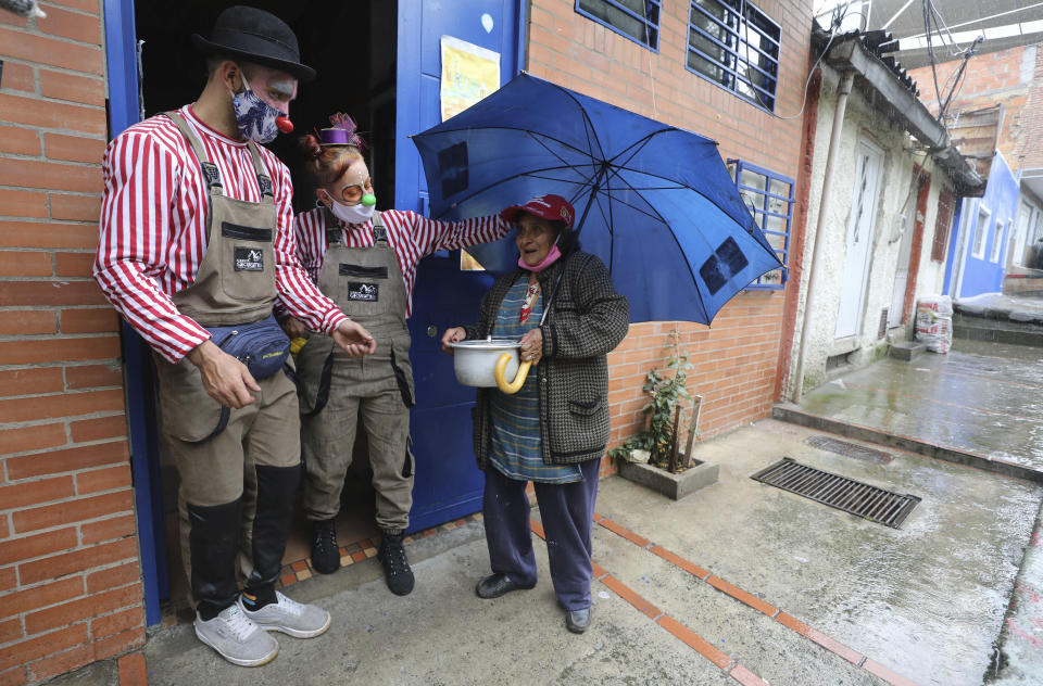 Troupe members of "Circo Encuentro" deliver a pot of soup to a resident that they prepared with donated food items, in Bogota, Colombia, Saturday, July 4, 2020. The troupe cooks up a "sopita de murcielago" or bat soup community kitchen style in a selected neighborhood for residents who have been economically affected by the COVID-19 related shutdowns. (AP Photo/Fernando Vergara)