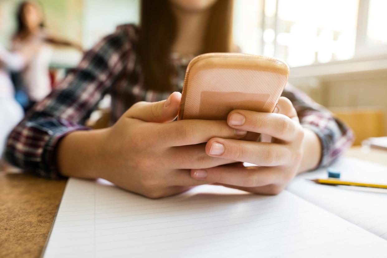 Close-up of girl typing text message on cell phone at the desk in the classroom.