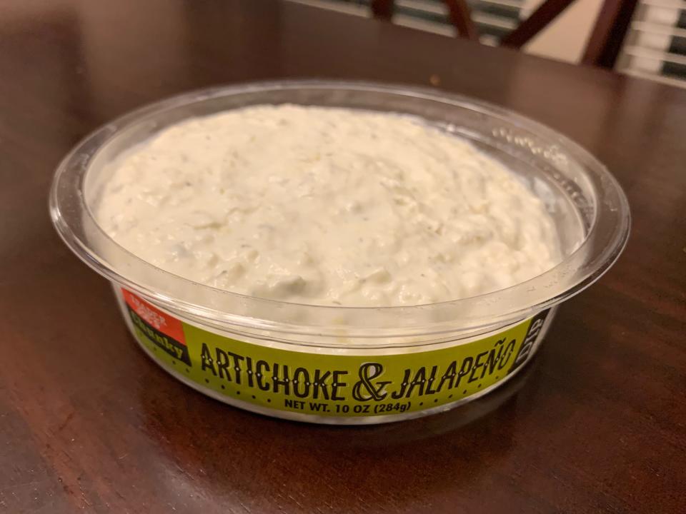 open green tub of trader joe's artichoke and jalepeno dip on wood table