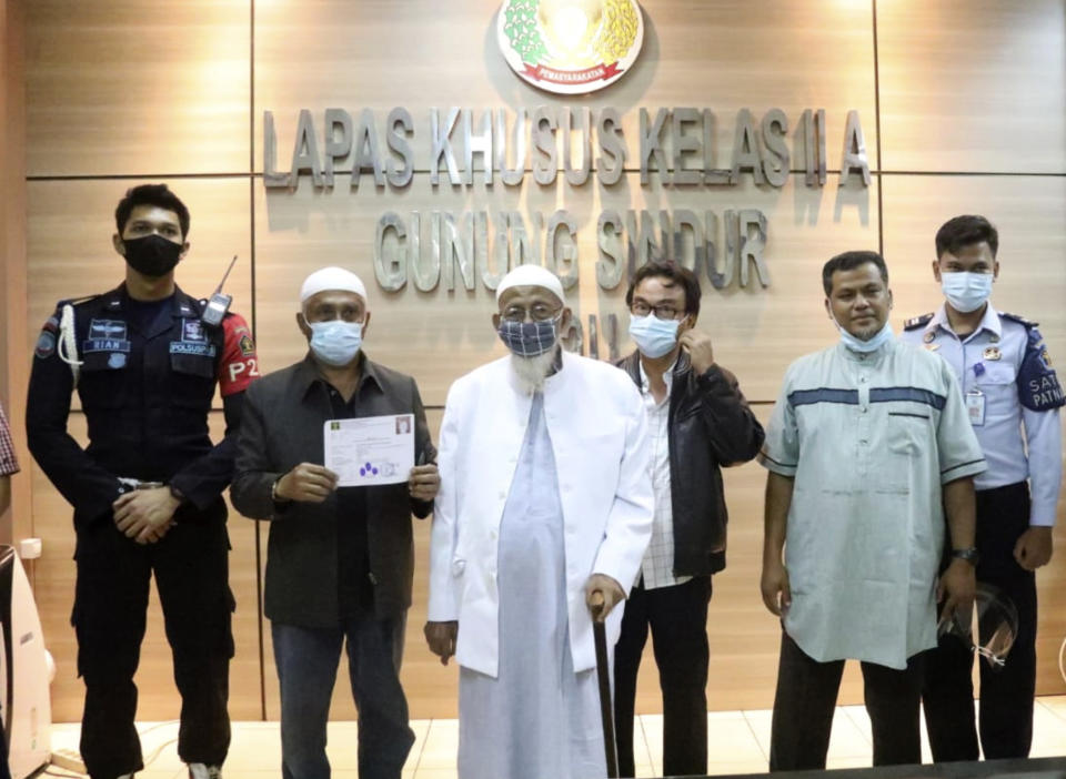 CORRECTS SON'S SPELLING - In this photo release by Correctional Facilities Directorate General of Indonesian Justice Ministry, Islamic cleric Abu Bakar Bashir, center left, poses for a photo with lawyers, prison staff and his son Abdul Rohim, second right, before leaving Gunung Sindur prison upon his release, in Bogor, West Java, Indonesia, Friday, Jan. 8, 2021. Convicted firebrand cleric who inspired the Bali bombers and other violent extremists walked free from an Indonesian prison Friday after completing his sentence for funding the training of Islamic militants. (Correctional Facilities Directorate General via AP Photo)