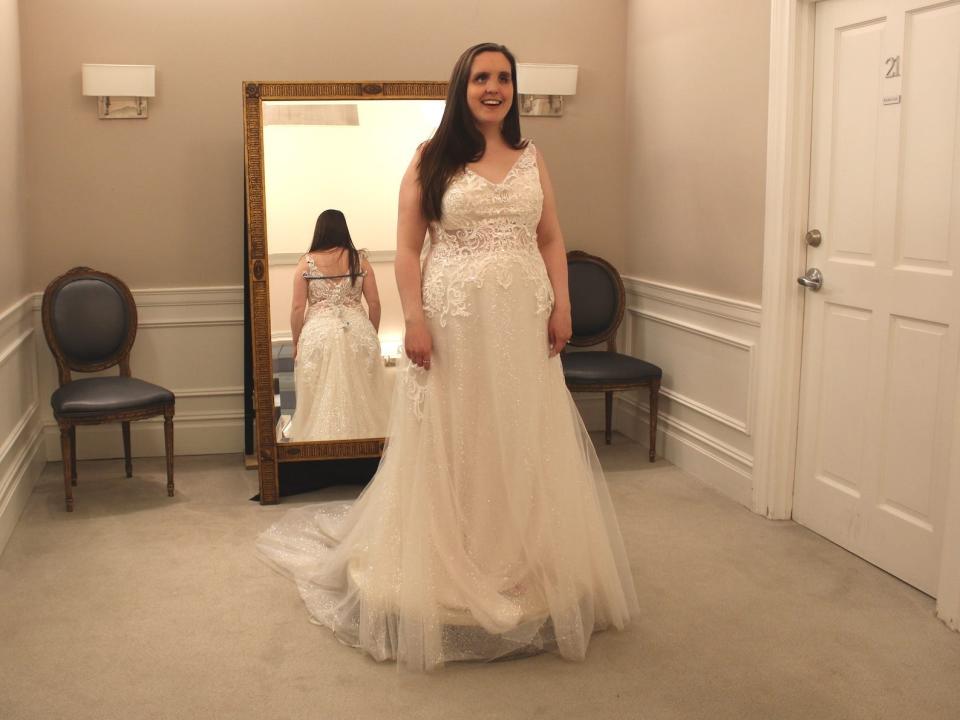 A bride stands on a pedestal in a wedding dress in a bridal store.