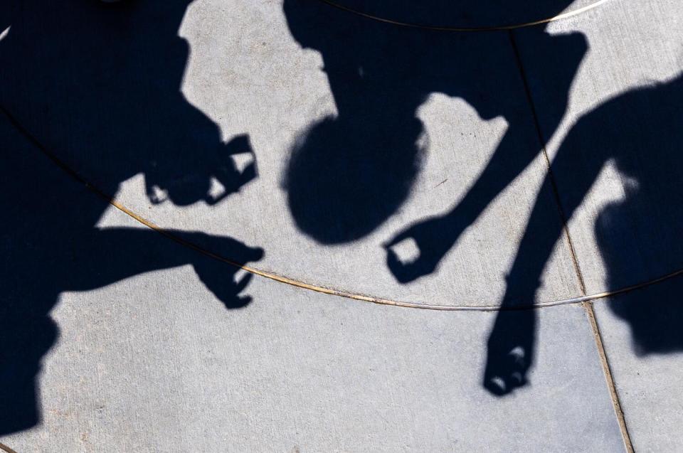 Solar eclipse watchers cast crescent-shaped shadows of the eclipse on a sidewalk.