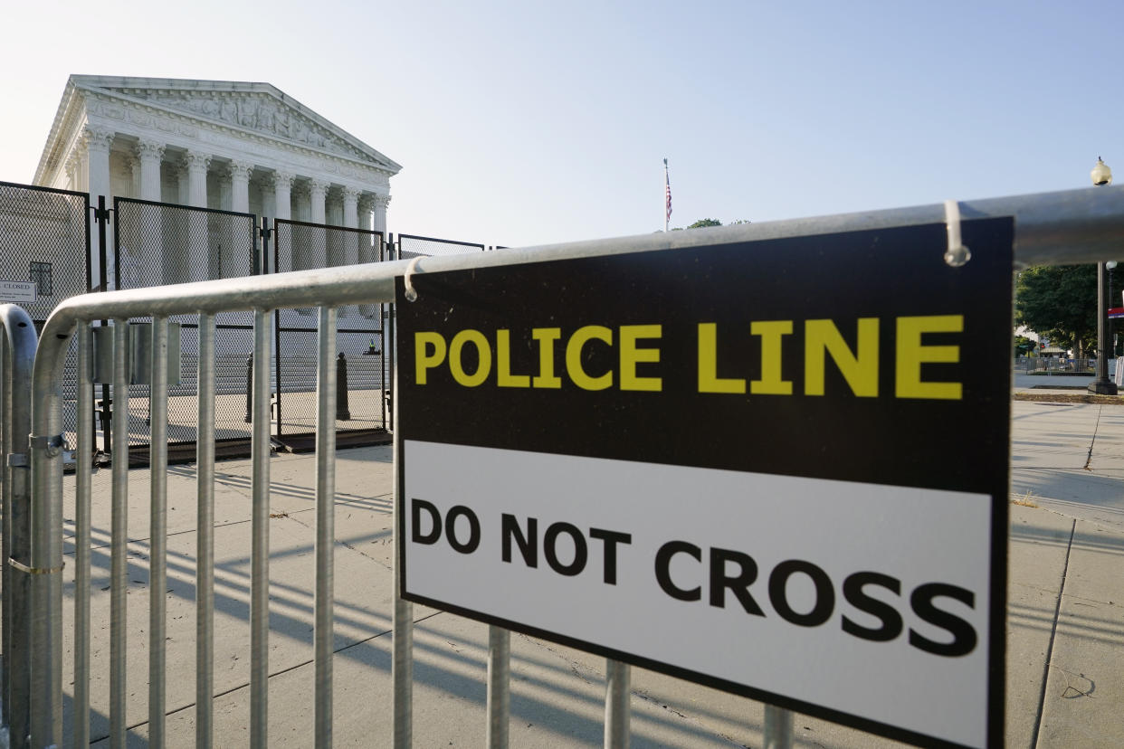The Supreme Court is seen behind fencing and a barricade. A sign on the barricade reads: Police line: Do not cross.