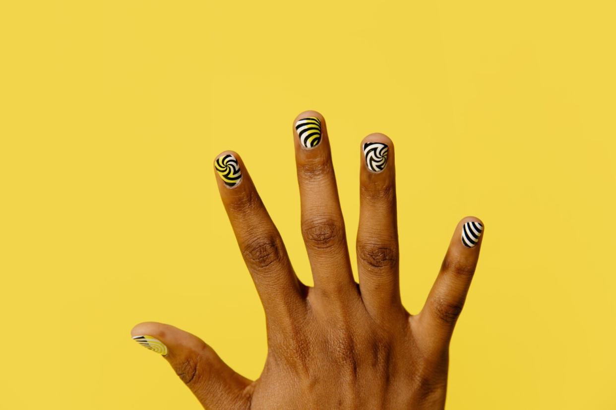 black person's hand with swirl nail designs on yellow background