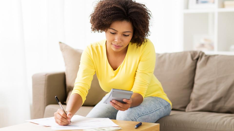 budget, finances and people concept - african american woman with papers and calculator counting money at home.