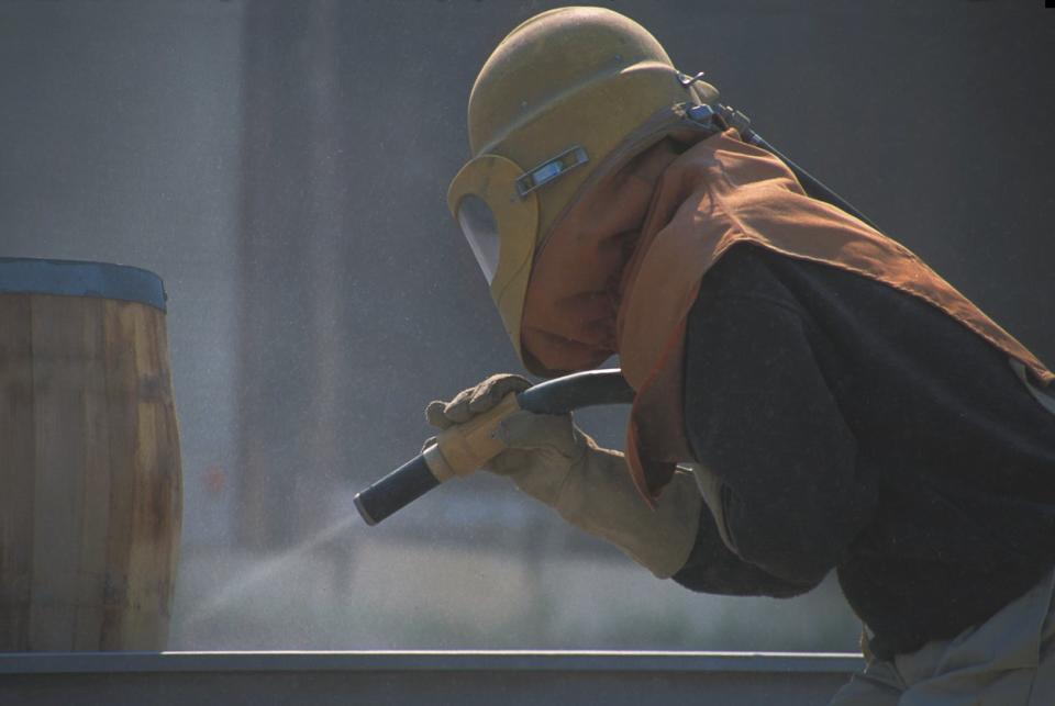 A worker uses a sandblasting tool.