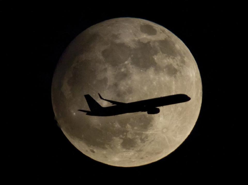 In this picture made available Friday, April 26, 2013, a passenger airplane is about to land at the airport in Frankfurt, Germany, thereby passing the moon which is clearly visible at night.