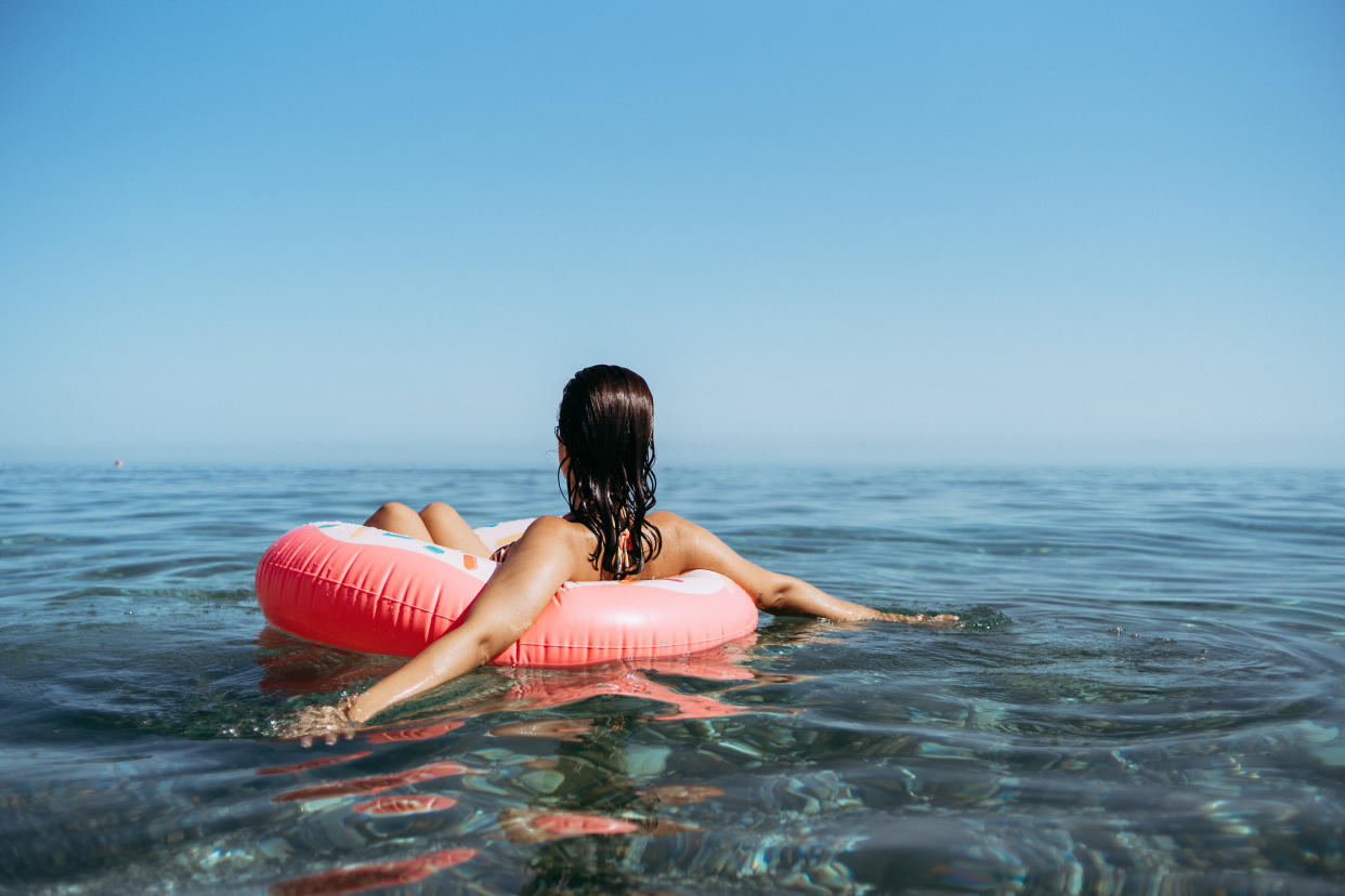 A girl drifts on a body of water in an orange tubelike flotation toy.