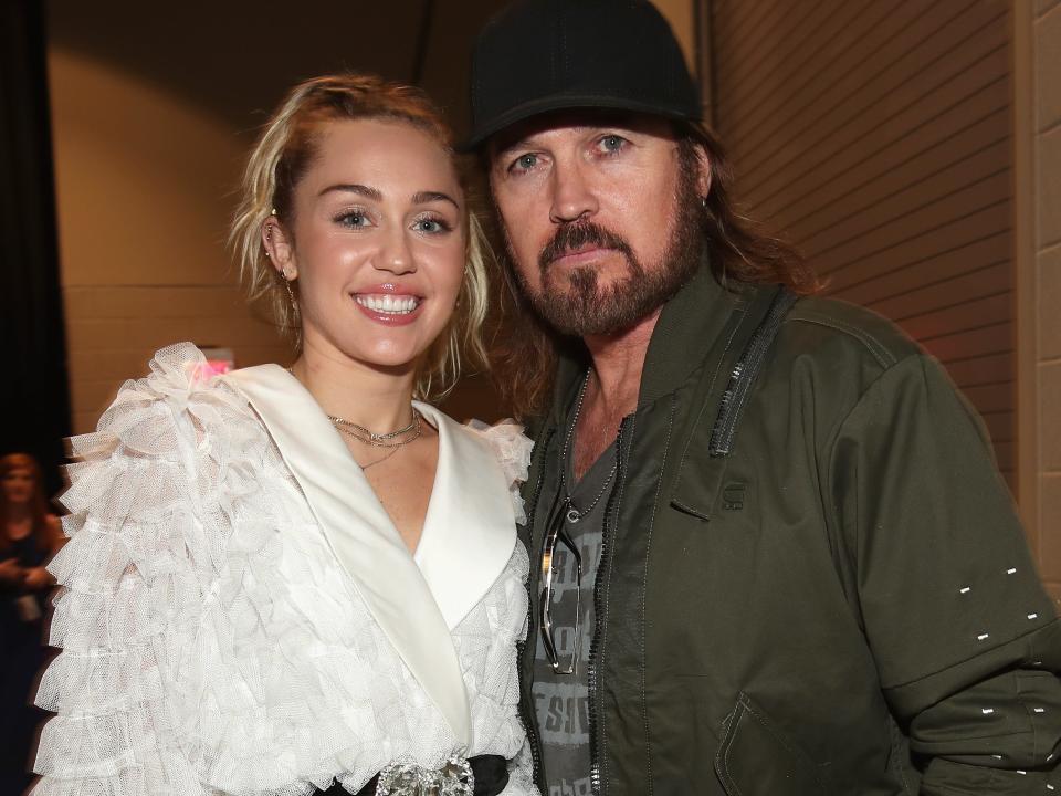 Miley Cyrus in a white dress, Billy Ray Cyrus in a green jacket