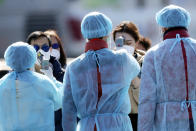 Officials in protective suits ensure the temperature of foreign passengers disembarked from the quarantined Diamond Princess cruise ship before boarding to buses at a port in Yokohama, near Tokyo, Friday, Feb. 21, 2020. Passengers tested negative for COVID-19 started disembarking since Wednesday. (AP Photo/Eugene Hoshiko)