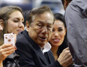 In this photo taken on Friday, Oct. 25, 2013, Los Angeles Clippers owner Donald Sterling, center, and V. Stiviano, right, watch the Clippers play the Sacramento Kings during the first half of an NBA basketball game, in Los Angeles. The NBA is investigating a report of an audio recording in which a man purported to be Sterling makes racist remarks while speaking to Stiviano. NBA spokesman Mike Bass said in a statement Saturday, April 26, 2014, that the league is in the process of authenticating the validity of the recording posted on TMZ's website. Bass called the comments "disturbing and offensive." (AP Photo/Mark J. Terrill)