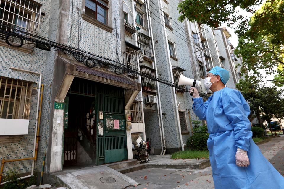 In this photo released by China's Xinhua News Agency, a volunteer uses a megaphone to talk to residents at an apartment building in Shanghai, China, Tuesday, April 12, 2022.