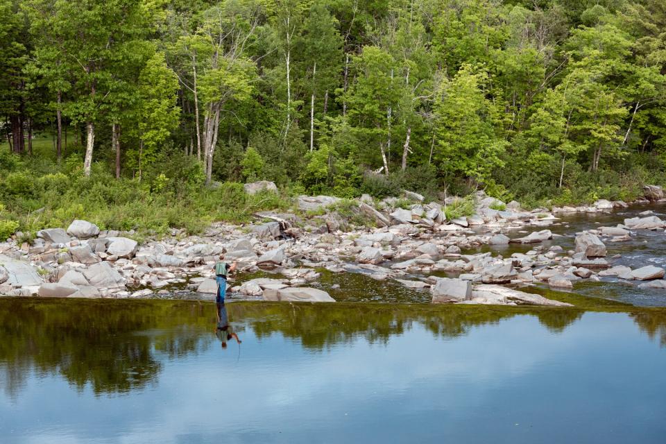 A man standing and fly fishing on the dam across the Carrabassett River in Kingfield, Maine.