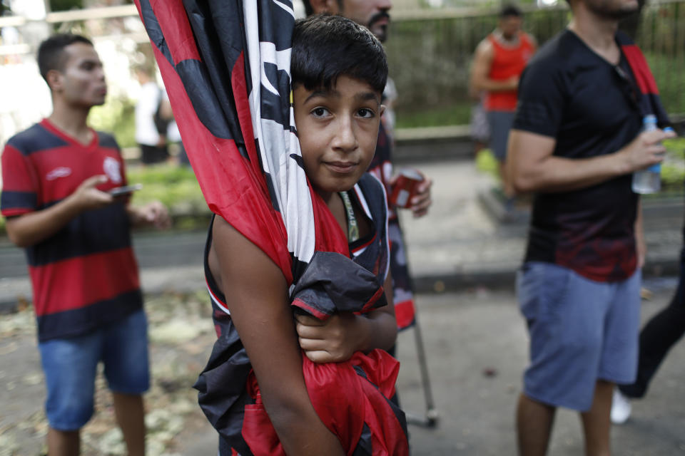 A boy holds a Flamengo soccer team flag as fans gather to honor the teenage players killed by a fire, in Rio de Janeiro, Brazil, Saturday, Feb. 9, 2019. A fire early Friday swept through the sleeping quarters of an academy for Brazil's popular professional soccer club Flamengo, killing several and injuring others, most likely teenage players, authorities said. (AP Photo/Silvia Izquierdo)