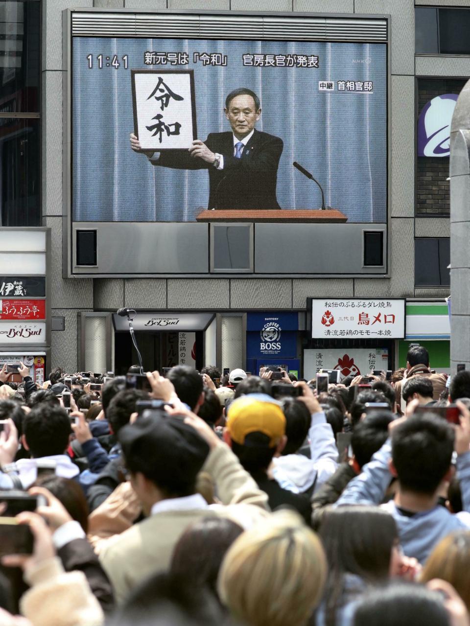 People gather to watch a huge screen which airs a live footage of a press conference by Chief Cabinet Secretary Yoshihide Suga, in Osaka Monday, April 1, 2019. The name of the era of Japan's soon-to-be-emperor Naruhito will be "Reiwa," the government announced Monday. (Takaki Yajima/Kyodo News via AP)