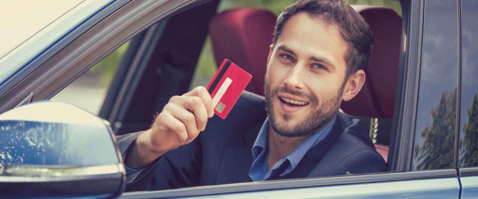 Happy smiling man sitting inside his new car showing credit card. Personal transportation auto purchase concept