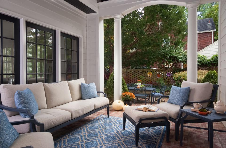 The large patio is filled with metal-framed furniture and slate-blue hues. Though the space is covered, the cushions feature outdoor fabric to withstand all types of weather. A complementary rug pulls the look together, while urns full of bright flowers add different pops of color. A few steps lead down toward the exposed patio area, which offers additional seating in a similar color scheme.