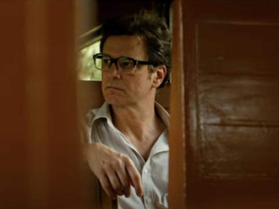 Colin Firth wearing glasses while riding on a train.