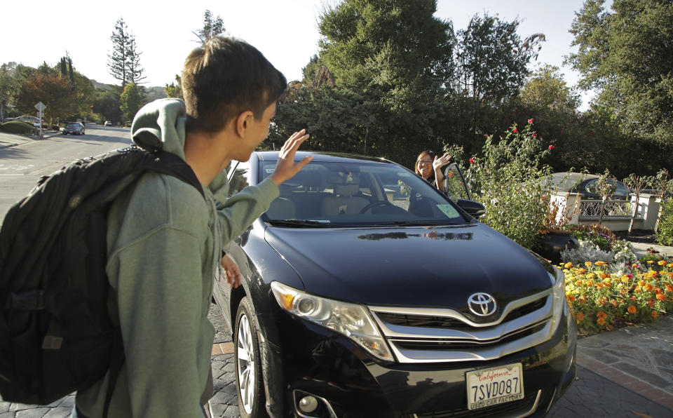 In this photo taken Tuesday, Oct. 29, 2019, Zum driver Stacey Patrick, right, waves goodbye to student Saahas Kohli, left, as he returns home from school in Saratoga, Calif. A handful of ride-hailing companies have surfaced that allow parents to order rides, and in some cases childcare, for children using smartphone apps. The promise is alluring at a time when children are expected to accomplish a dizzying array of extracurricular activities and the boundaries between work and home have blurred. But the companies face hurdles convincing parents that a stranger hired by a ride-hailing company is trustworthy enough to ferry their most precious passengers. (AP Photo/Ben Margot)