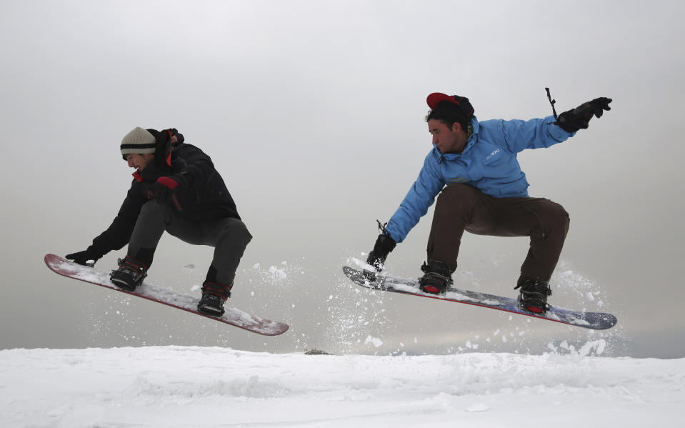 In this Friday, Jan. 24, 2020 photo, Ahmad Sorush, 22, left, and Nizaruddin Alizada, 20, make a jump on the snow-covered hillside known as Kohe Koregh, on the outskirts of Kabul, Afghanistan. While Afghanistan’s capital may seem an unlikely destination for snowboarders, a group of young Afghans is looking to put the city on the winter sports map and change perceptions about their war-weary nation. (AP Photo/Rahmat Gul)