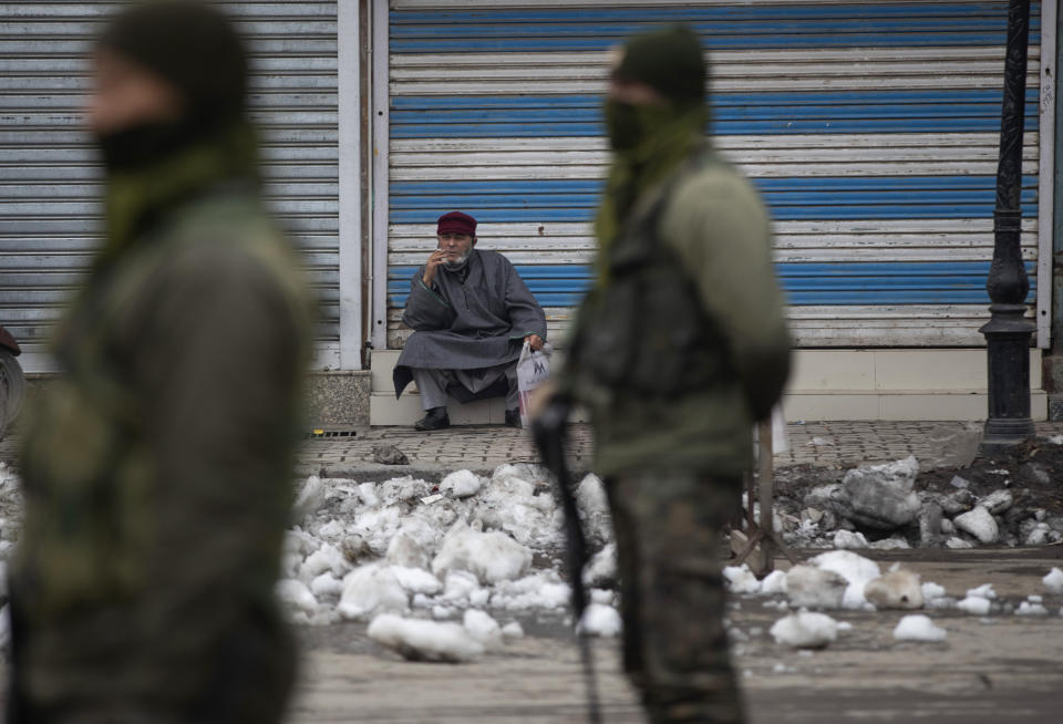 Indian paramilitary soldiers stand guard as a Kashmiri man smokes outside a closed shop in Srinagar, Indian controlled Kashmir, Tuesday, Feb. 9, 2021. Businesses and shops have closed in many parts of Indian-controlled Kashmir to mark the eighth anniversary of the secret execution of a Kashmiri man in New Delhi. Hundreds of armed police and paramilitary soldiers in riot gear patrolled as most residents stayed indoors in the disputed region’s main city of Srinagar. (AP Photo/Mukhtar Khan)