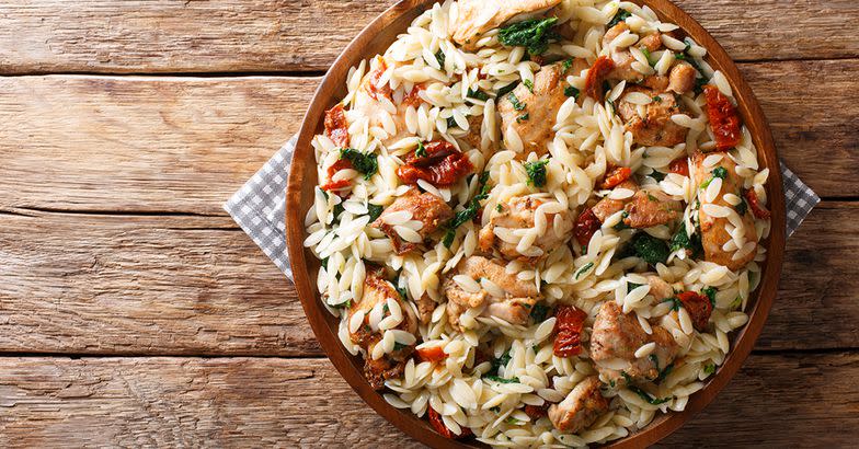 Italian pasta orzo with grilled chicken, dried tomatoes, spinach and cheese close-up on the table. horizontal top view from above