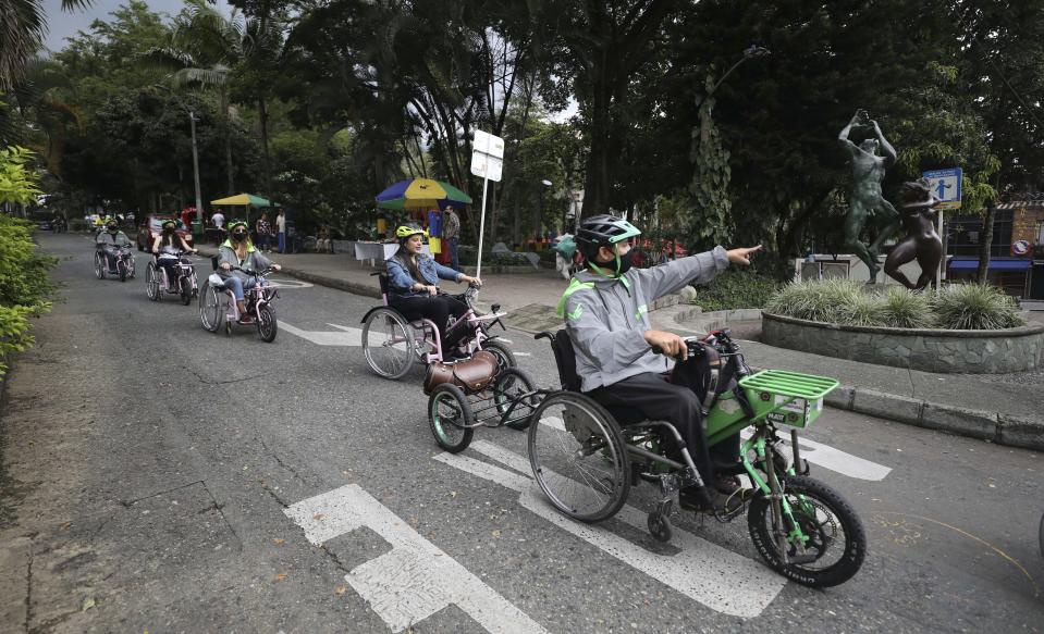 Wilson Guzman, a tour guide, right, leads an electric wheelchair tour in Medellin, Colombia, Wednesday, Nov. 18, 2020. For the equivalent of $25, both people who can and can't walk can get on the electric wheelchairs and take the three-hour tour of the city’s riverside parks, which includes stops at a coffee shop and a bar that does beer tasting. (AP Photo/Fernando Vergara)