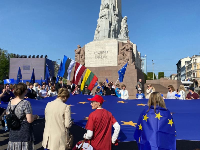 On the 20th anniversary of Latvia's accession to the EU, people hold a huge EU flag in front of the Freedom Monument.  Alexander Welscher/dpa