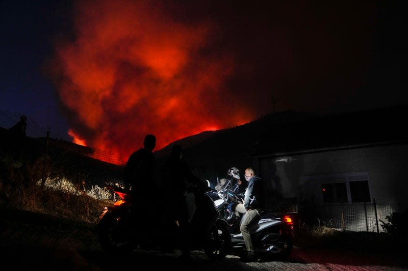 Men on motorcycles watch a fire at Penteli, Greece, on Tuesday, July 19, 2022.