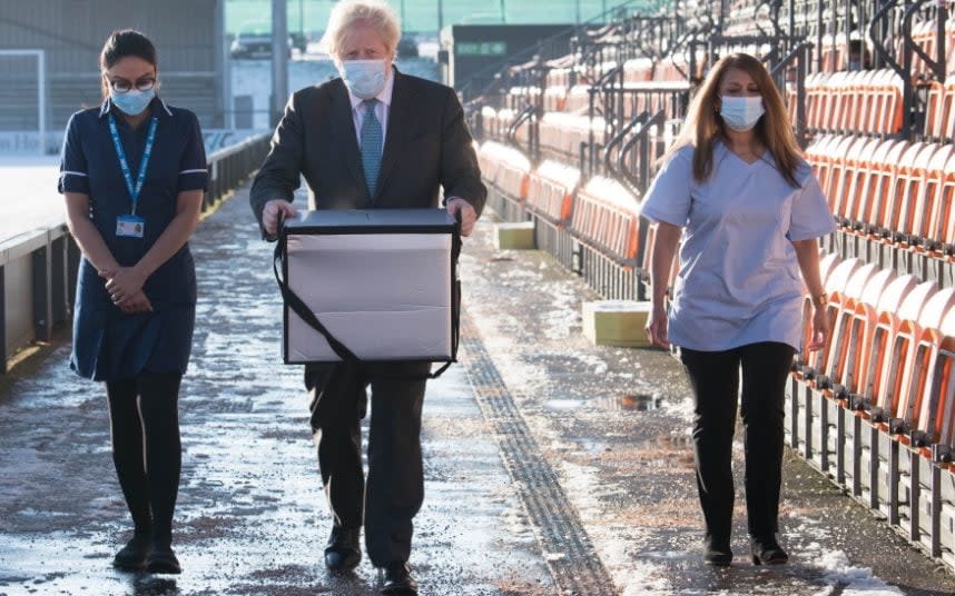 Boris Johnson carries doses of the AstraZeneca jab at a vaccination centre at Barnet FC - PA