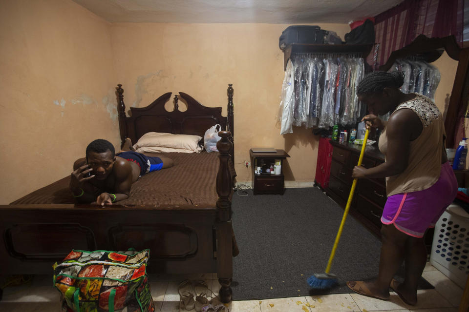 Deportees Jhon Celestin lies on a bed as he talks on the phone, while his wife Delta De Leon sweeps the floor of their temporary bedroom, in a relative's home in Port-au-Prince, Haiti, Thursday, Sept. 23, 2021. The couple are among the more than 1,900 migrants that the U.S. expelled to Haiti this week. (AP Photo/Joseph Odelyn)