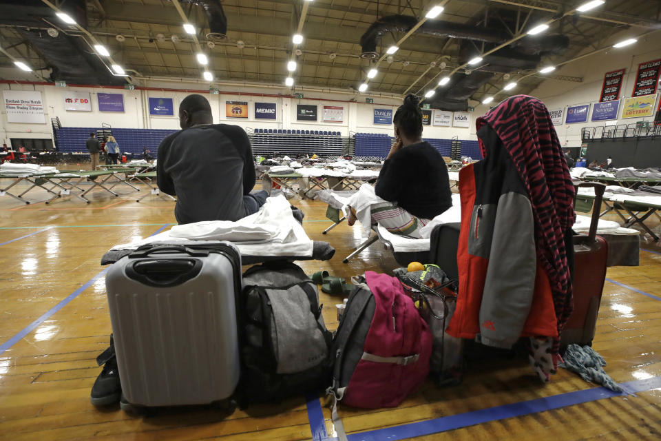 In this June 13, 2019 photo, a migrant couple sit with their belongings inside the Portland Exposition Building in Portland, Maine. Maine's largest city has repurposed the basketball arena as an emergency shelter in anticipation of hundreds of asylum seekers who are headed to the state from the U.S. southern border. Most are arriving from Congo and Angola. (AP Photo/Elise Amendola)