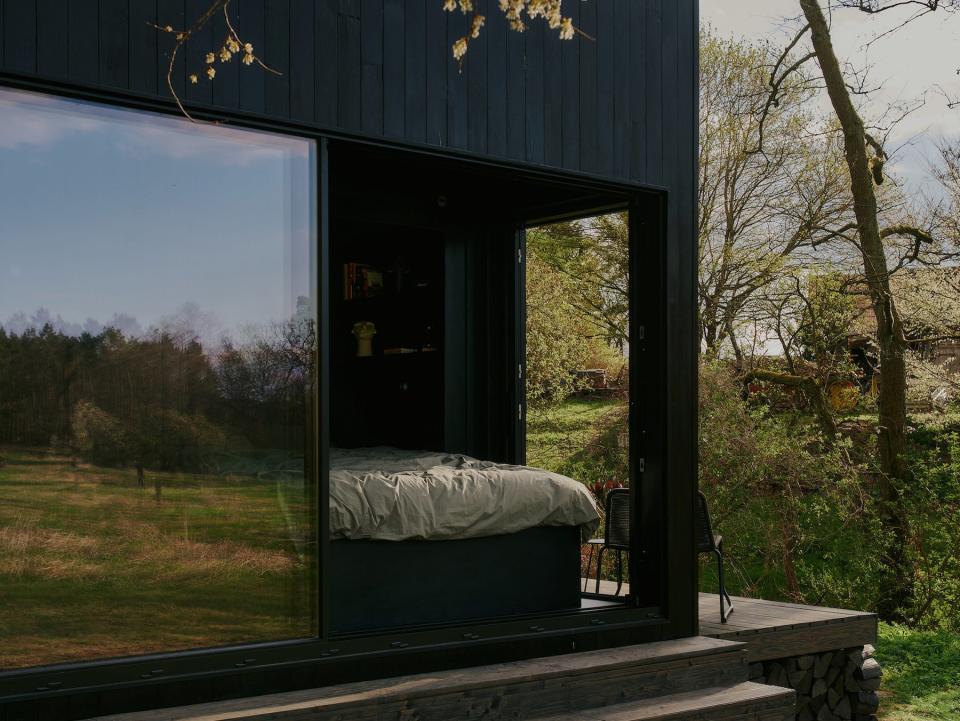 A close up of a Raus cabin in nature surrounded by trees and open fields.