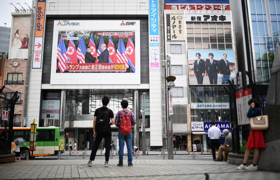 Pedestrians in Tokyo look at a wall-mounted screen displaying live news of the meeting between Trump and Kim on June 12, 2018.