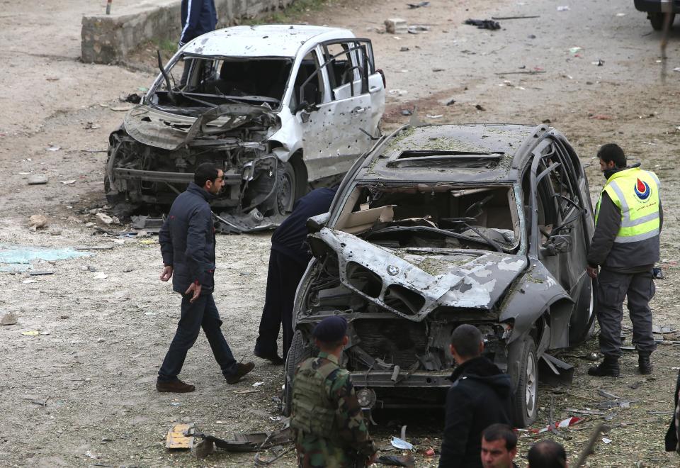 A Hezbollah civil defense worker, right, checks a damaged car at the site of a deadly car bombing Sunday night, in the town of Nabi Othman, about 30 kilometers (18 miles) north of Baalbek, northeast Lebanon, Monday March 17, 2014. Lebanese security officials said the explosion killed at least two people and caused panic and massive destruction in the Hezbollah stronghold, which has a sizable Christian population in addition to Shiites. The civil war in neighboring Syria already has ignited polarizing sectarian tensions between Lebanon's Sunnis and Shiites. (AP Photo/Hussein Malla)