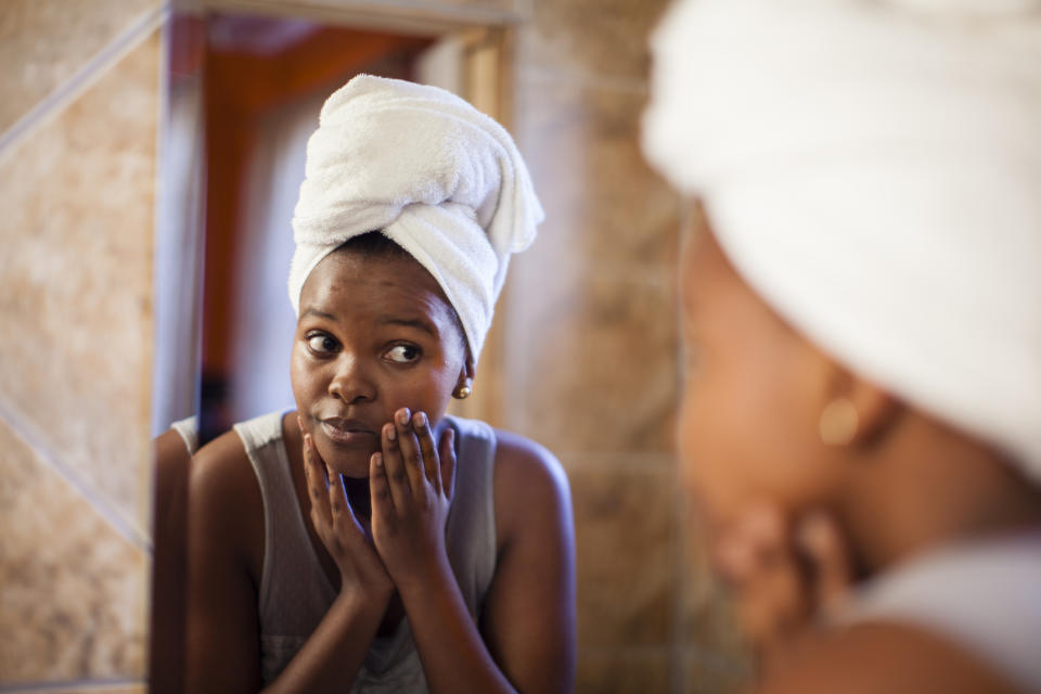 Young woman checks skin in mirror. Image: Getty
