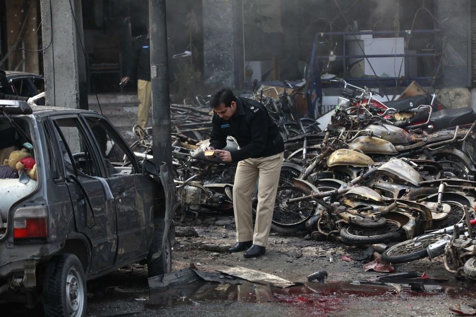 A policeman uses a mobile phone to take pictures of the damage at the site of an explosion outside the police headquarters, in Lahore