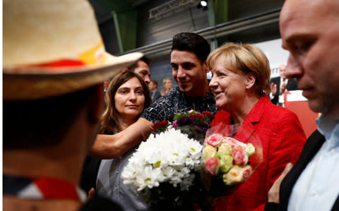 Syrian refugees offer flowers to German Chancellor and Christian Democratic Union's (CDU) main candidate Angela Merkel - Credit: ODD ANDERSEN/AFP/Getty Image