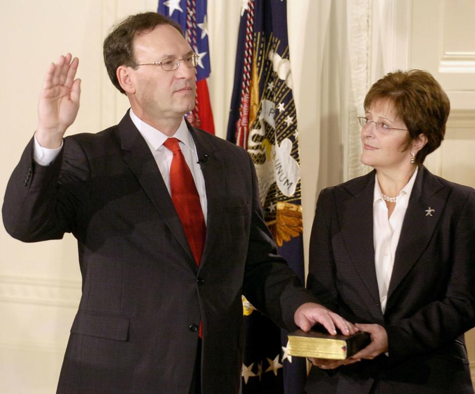 Samuel Alito raises his hand as he is sworn into the Supreme Court. His wife, Martha Ann holds the bible next to him. 