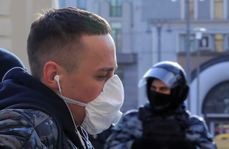 A man wearing a protective mask walks past a law enforcement officer in central Moscow