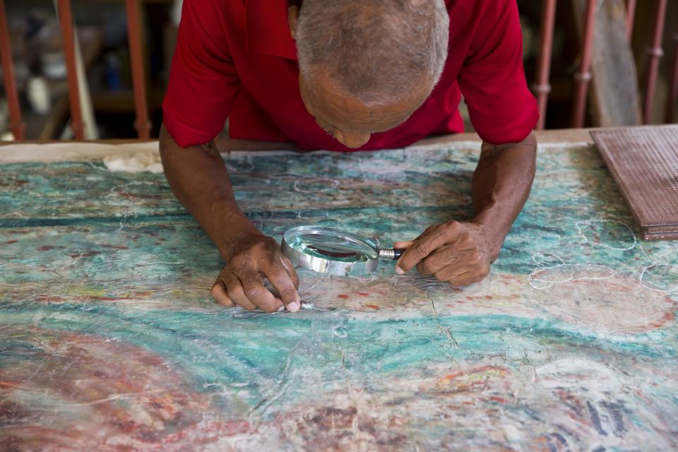 In this July 1, 2019 photo, Haitian artist Franck Louissaint works on the painstaking renovation of a painting by Haitian artist Robert Saint Bruce, at the Musée d'Art du Collège Saint Pierre, in Port-au-Prince, Haiti. The earthquake ravaged museum, which used to draw 9,000 visitors a year, is tucked into the southeast corner of Port-au-Prince's historic area and features mostly donated artwork. (AP Photo/Dieu Nalio Chery)