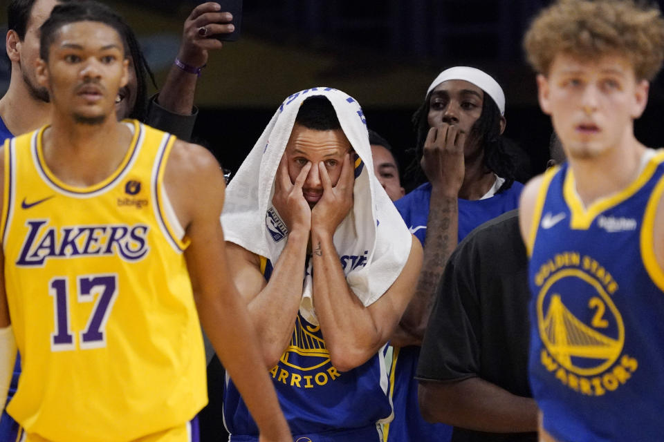 Golden State Warriors guard Stephen Curry, center, watches from the bench as Los Angeles Lakers forward Alex Fudge, left, and forward Jarred Vanderbilt, right, play the closing seconds of an NBA preseason basketball game Friday, Oct. 13, 2023, in Los Angeles. (AP Photo/Mark J. Terrill)