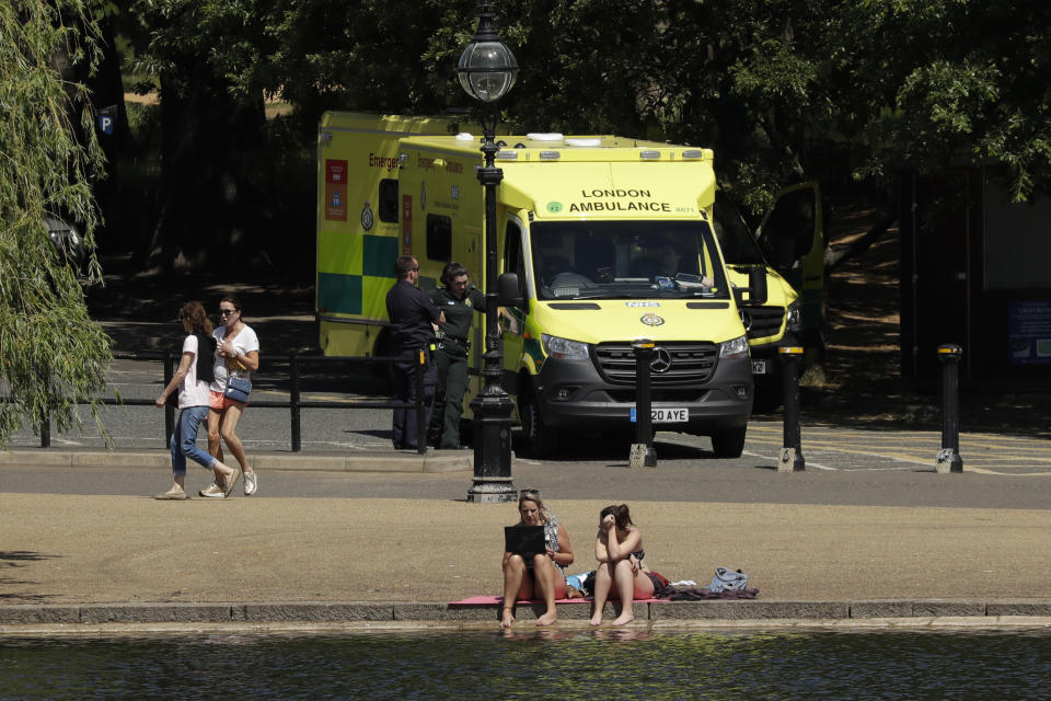 Two ambulances stand parked in a car park as people relax during warm weather by the Serpentine lake, in Hyde Park, London, Wednesday, May 20, 2020. Lockdown restrictions due to the coronavirus outbreak have been relaxed allowing unlimited outdoor exercise and activities such as sunbathing. The UK's Met Office said Wednesday, it is the hottest day of the year so far with 27.8 Celsius recorded at Heathrow. (AP Photo/Matt Dunham)