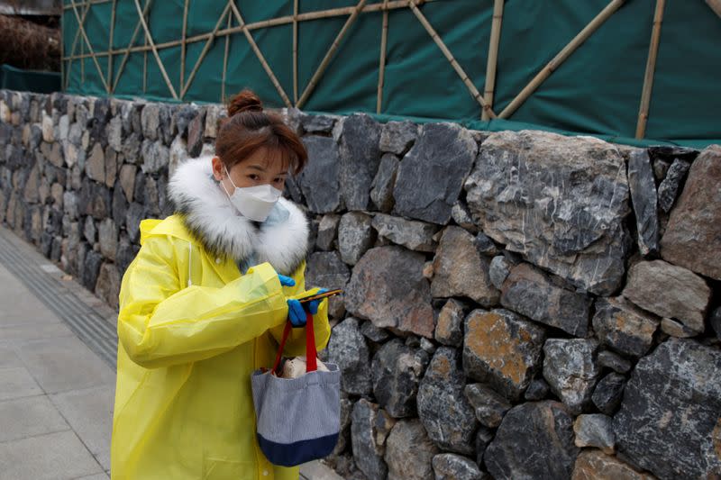 A woman wearing a face mask, raincoat and rubber gloves walks on the street in Beijing as the country is hit by an outbreak of the novel coronavirus